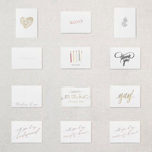 Display of twelve different white cards. Gold foil hear comprised of flowers, Xoxo in rose gold foil, greyscale leafy plant, congrats embossed in white, happy birthday printed underneath five candles of varying colors, Thank You in grey script writing, Thinking of you, I couldn't tie the know without you in gold, Yay! in gold foil, will you be my bridesmaid in rose gold, will you be my maid of honor in rose gold foil, will you be my matron of honor in rose gold foil.