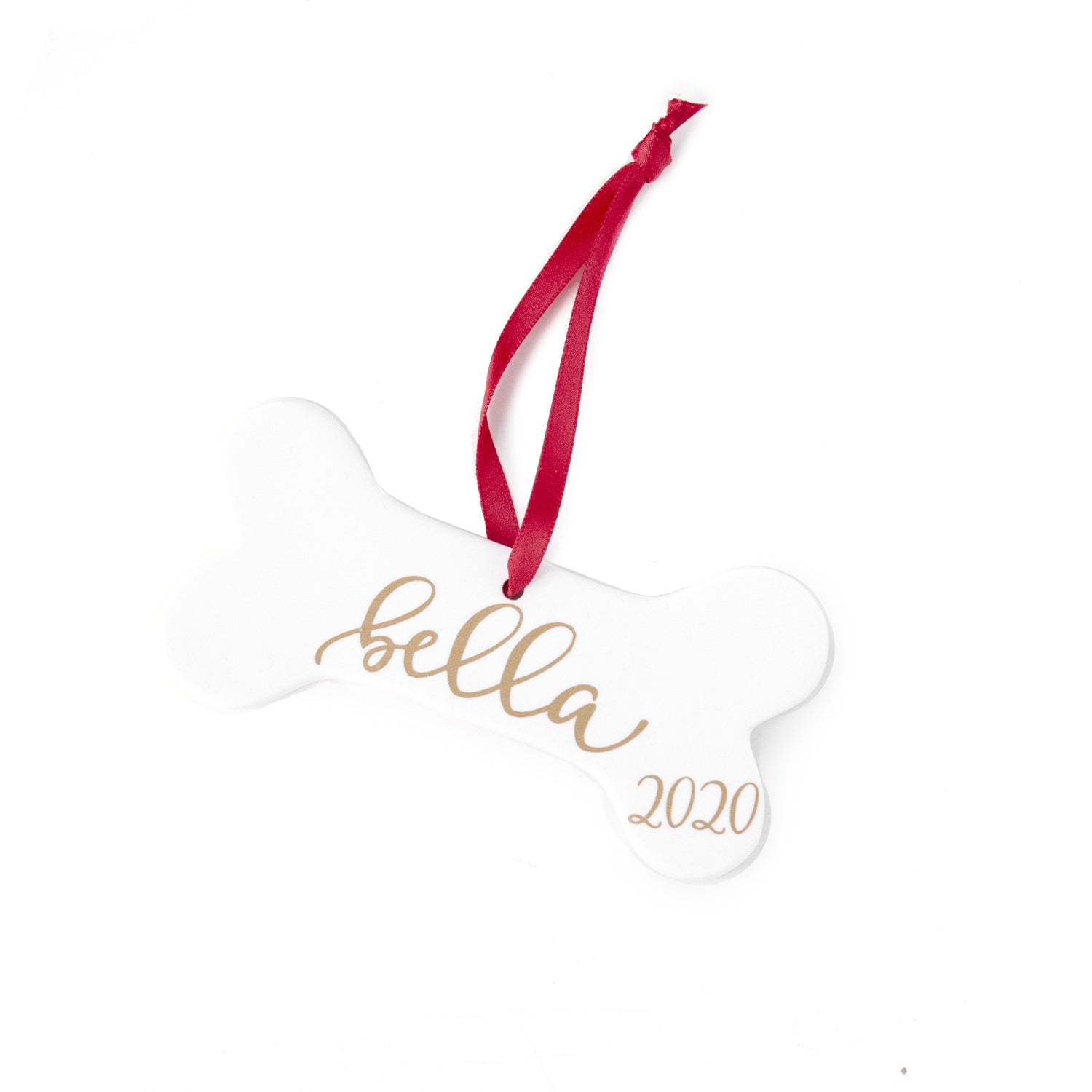 White ceramic dog bone ornament personalized in gold lettering with Bella and 2020 with a red ribbon, on a white background.