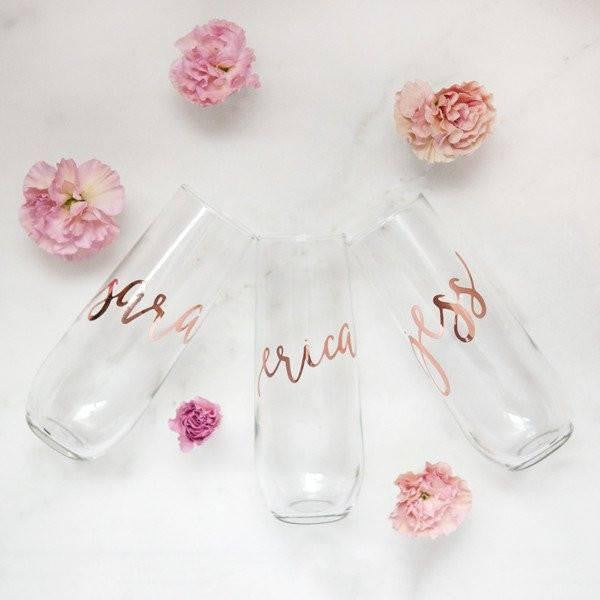 Three champagne flutes personalized in rose gold lettering with the names Sara, Erica, and Jess in a white background with five pink roses around them.