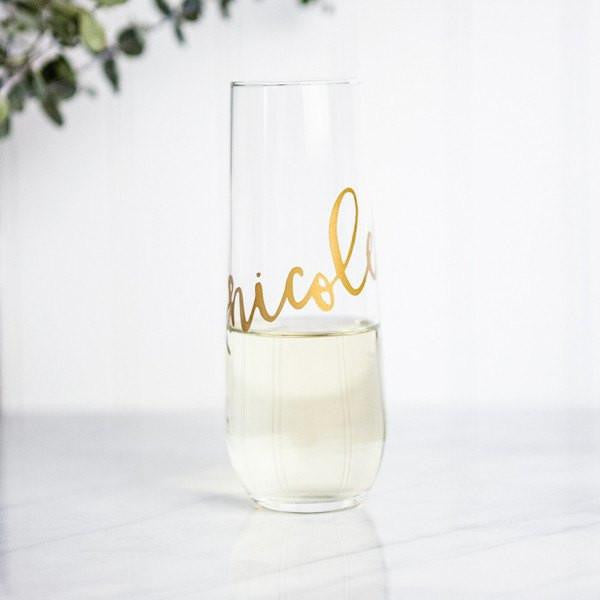 personalized champagne flutes, personalized transparent glass, personalized with the name Nicole in gold lettering in a white background with a green branch in the corner.  