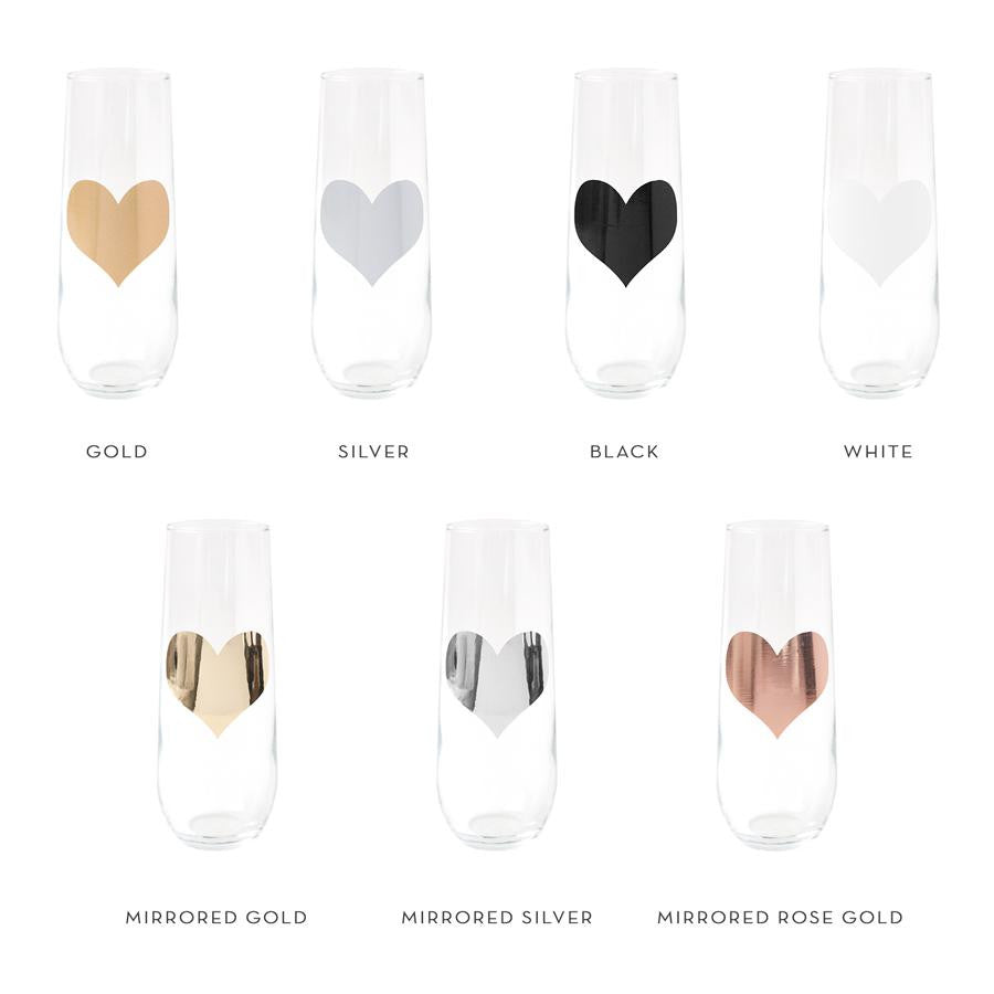 Seven stemless flute glasses with hearts displaying the sample colors of gold, silver, black, white, mirrored gold, mirrored silver and mirrored rose gold.