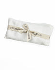 White, washed linen, 8.5" x 4", weighted eye pillow, Silk case filled with flaxseed and lavender on a white background tied with a beige ribbon with black lettering with the company's name FRoxblossom. 