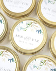 A close-up photograph presents several small, round, gold-colored containers, each adorned with a floral-themed label featuring the names "Jen & Vik" and the date "July 14, 2018."
