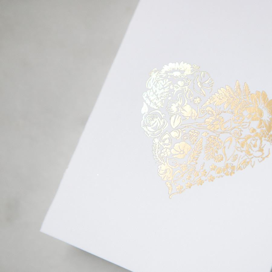 A simple yet elegant card, featuring a heart-shaped floral design rendered in gold foil, centered on a crisp white background.