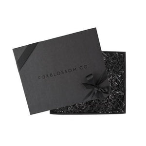 Black box embossed with foxblossom.co filled with black paper shred and tied with black ribbon. 