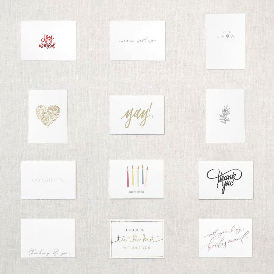 Display of twelve white cards. Gold floral heart, pink xoxo, gray branch, white congrats embossed, happy birthday under five candles, thank you in gray script, thinking of you, I couldn't tie the knot without you in gold, Yay! in gold script, will you be my bridesmaid rose gold, will you be my maid of honor rose gold, will you be my matron of honor rose gold