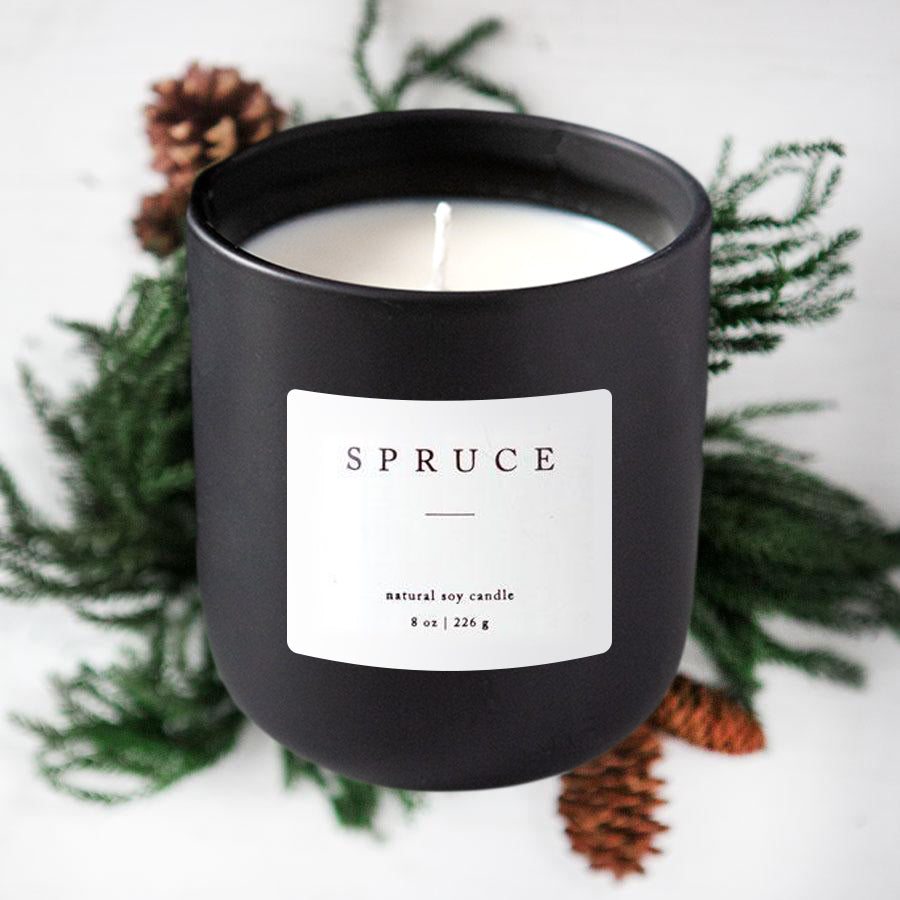 Spruce natural soy candle featured in its black jar container with a white with christmas branches background. 