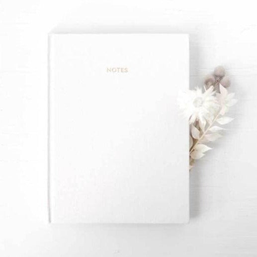White linen journal notebook featured on a white background with a dried flower bundle next to it. 
