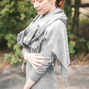Woman in an outdoor setting, wearing a grey dress and draped with a grey pashmina. 