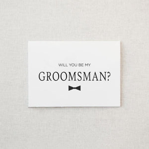 White envelope size card (approx. 3.5" x 5"), reads, "Will you be my groomsman?" in black text, with a bowtie graphic. 