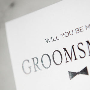 White envelope size card (approx. 3.5" x 5"), reads, "Will you be my groomsman?" in black text, with a bowtie graphic zoomed in.