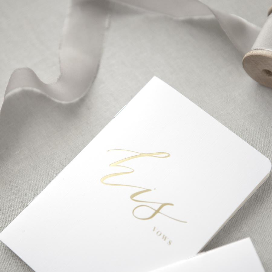 His foil stamped white vow book featured in a gray background.