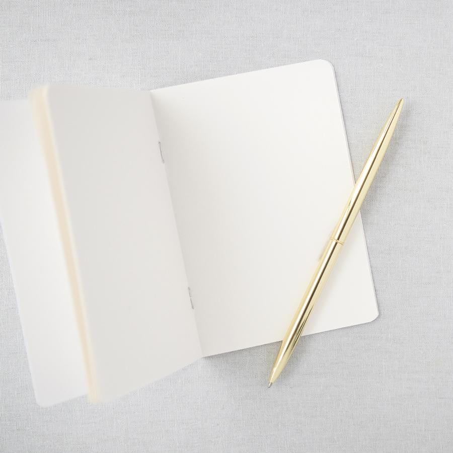 Vow book opened showing its white pages and a gold pen on top of it in a gray background. 