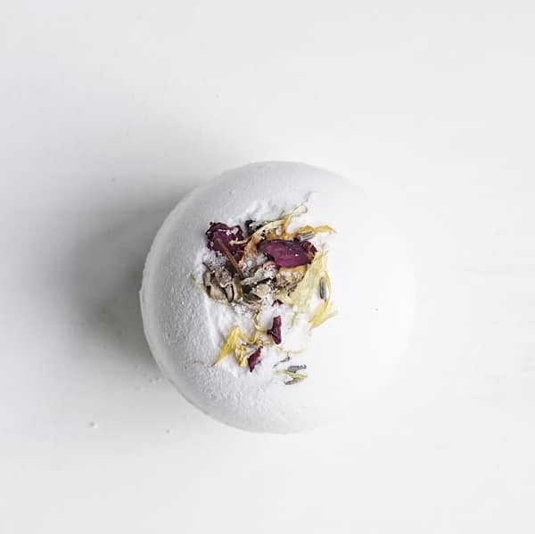 Among the flowers lavender essential oil bath bomb decorated with dried flower petals shown on a white background