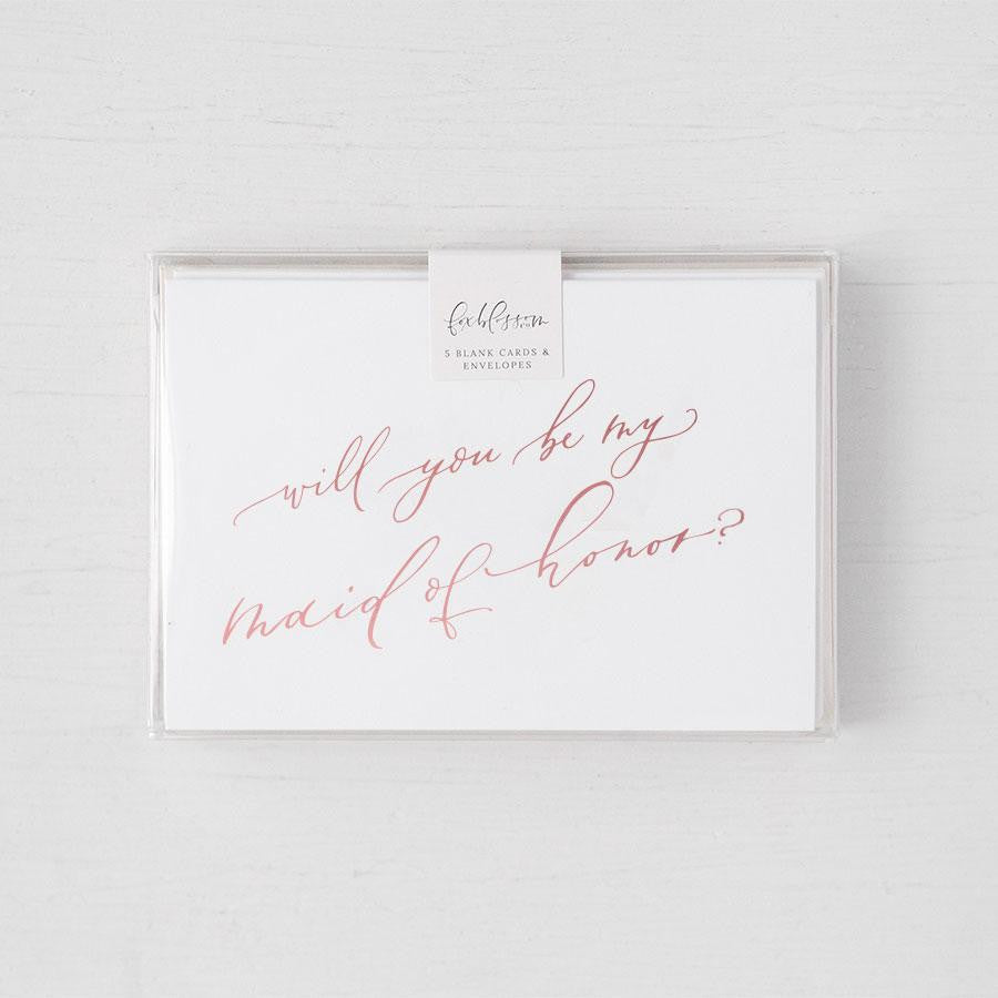 White envelope size card (approx. 3.5" x 5"), reads, "Will you be my maid of honor?" in rose gold text in a clear plastic bag.