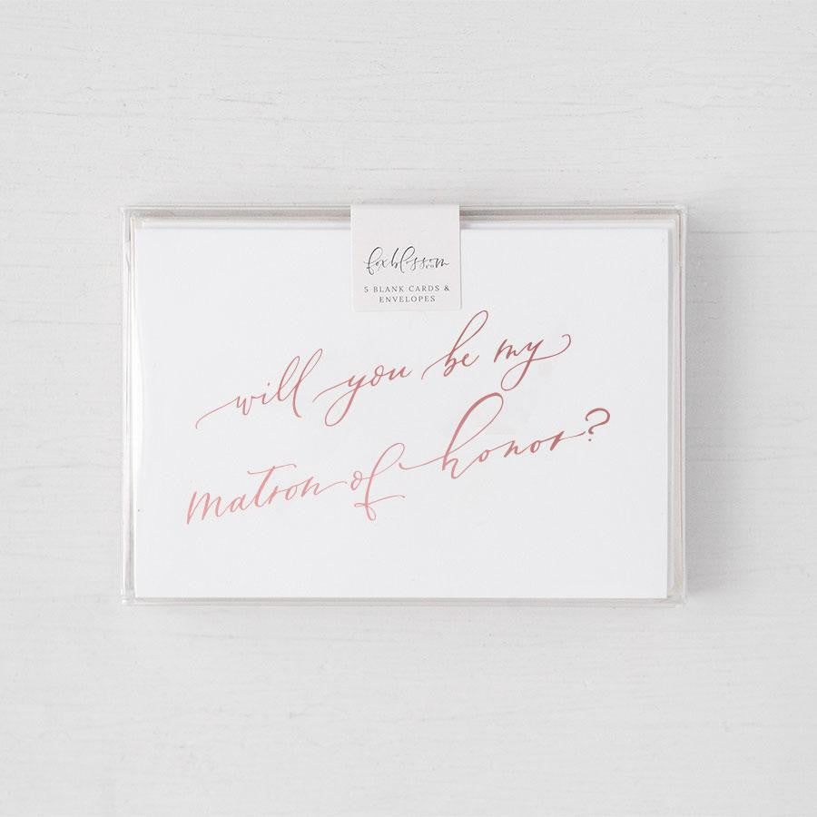 White envelope size card (approx. 3.5" x 5"), reads, "Will you be my maid of honor?" in rose gold text in a clear plastic bag. 
