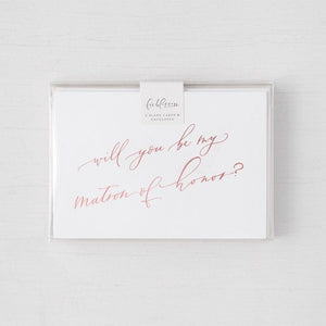 White envelope size card (approx. 3.5" x 5"), reads, "Will you be my maid of honor?" in rose gold text in a clear plastic bag. 