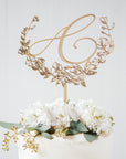 Monogram floral cake topper, featuring the monogram of the letter A  in gold on top of a cake on a white background.