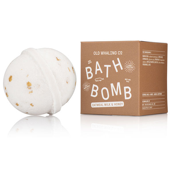 Old Whaling Co, Oatmeal milk & honey, bath bomb. Image shows the bath bomb unboxed  in its round  shape white with oatmeal pieces and it's box container next to it in brown color with white lettering. 
