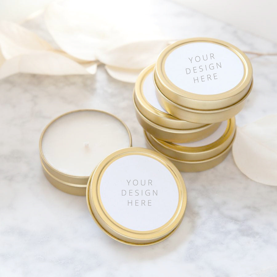 Your design here custom wedding favor candle shown 4 gold tins shown, 3 stacked up, one opened showing a white candle inside, they have a white round label with the words your design here in black lettering. 