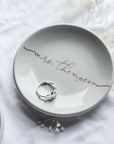 The image showcases our personalized  small, white ceramic ring dish with "mrs. Thompson" elegantly written in gold script, and a silver ring resting inside.