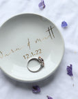 The image showcases our personalized  small, white ceramic ring dish with "Sara & Matt " and the date 12-1-22 elegantly written in gold script, and a silver ring resting inside.