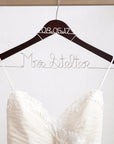 Dark wooden hanger with personalized date  08.05.17 in silver aluminum wire and base wire shaped into personalized name "Mrs Stelter" in silver. Holding a white wedding gown on a white background. 