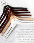 Hanger color variations. Matte black with silver hook, Dark wood with silver hook, Dark wood with gold hook, medium wood with silver hook, light wood with silver hook, white with silver hook, white with gold hook on a marble-like background.