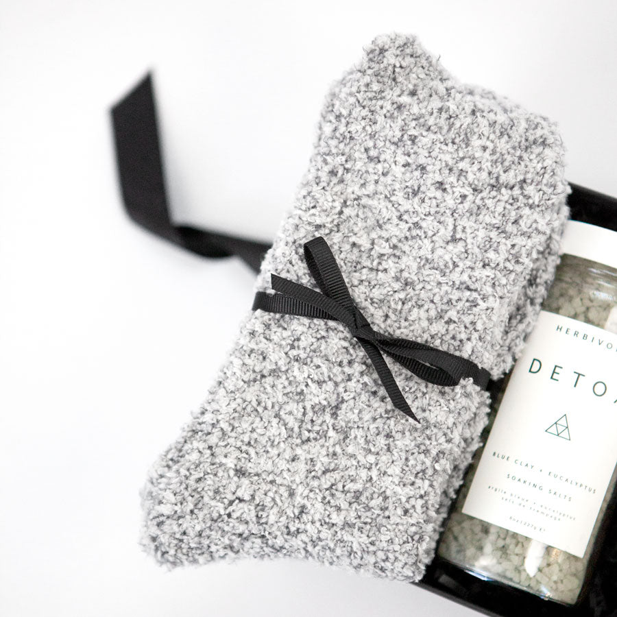 Gray &#39;foxblossom&#39; socks with a black ribbon, and &#39;herbivore&#39; detox soaking salts in a glass jar, placed in a small black &#39;foxblossom&#39; box with a black ribbon.