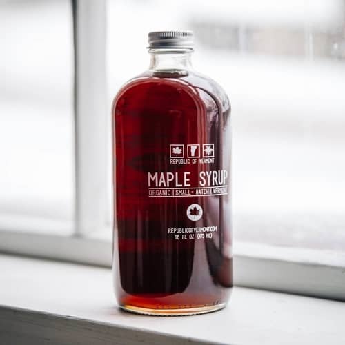 Republic of Vermont Maple Syrup showcased in it's clear jar that has a grey lid and white lettering with the information on a window ledge background. 