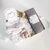 A light gray gifting box with a dried floral bundle, Slumberkins Slumber Sloth and hardback book, Chelsey Wang night night baby wash, a charcoal muslin swaddle and silicone and wooden teether.