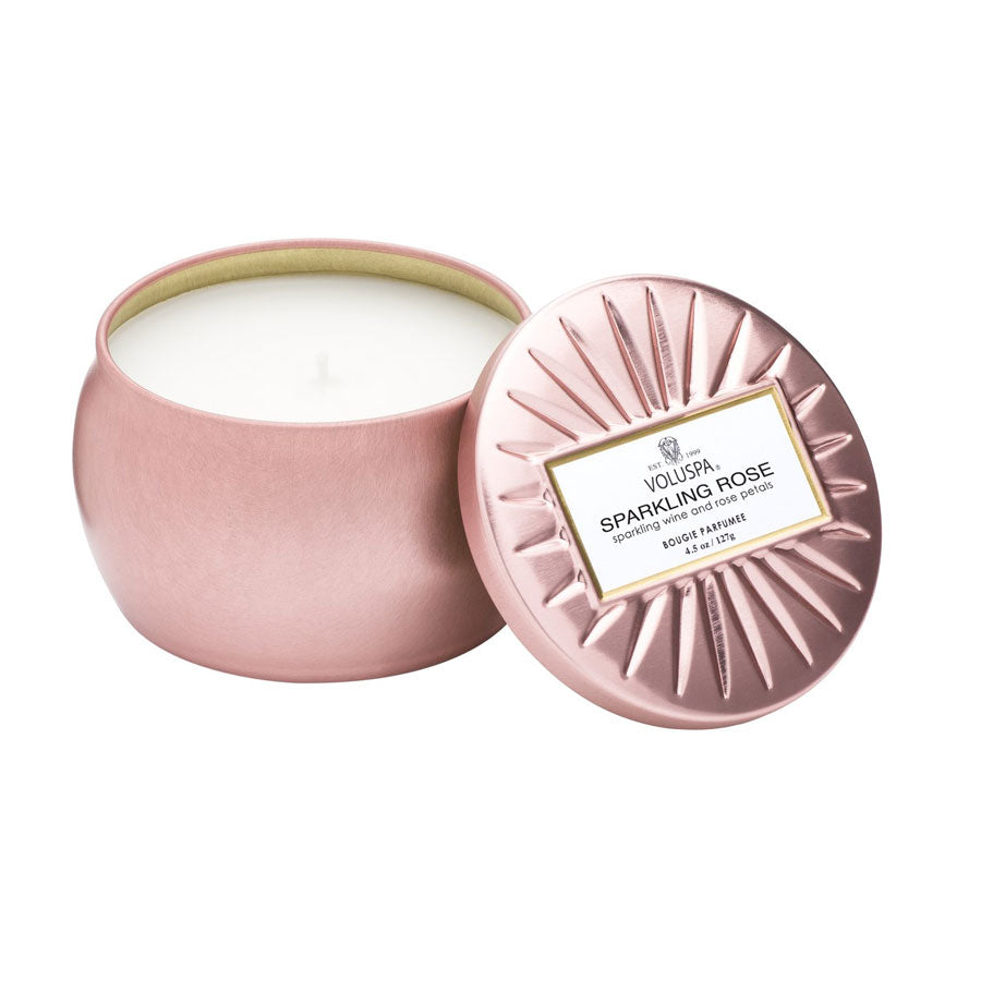 Metallic pink jar with lid removed and propped against the container showing a white candle inside.  