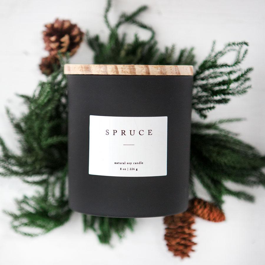 Spruce candle in its black jar with wooden lid in a Christmas background.