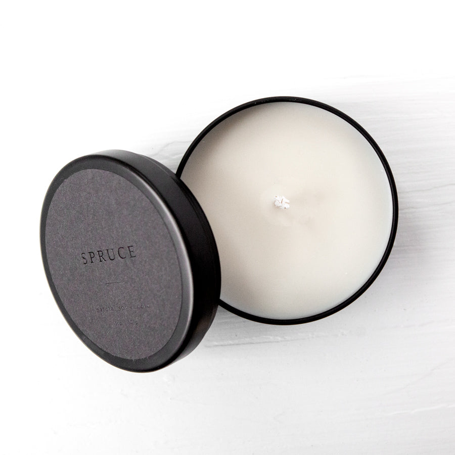 Spruce natural soy candle in its black tin container with grey label and black lettering featured. 