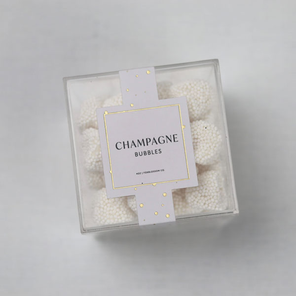 Sugarfina Champagne bubbles in their clear container showcasing the bubbles inside and the label black lettering with gold details. 