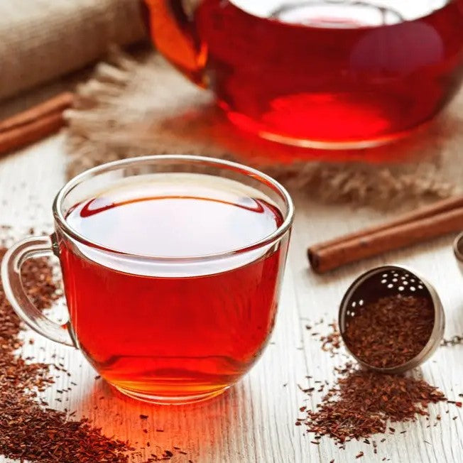 Image that shows a glass mug with the tea  in a background that has cinnamon, a tea mug semi full with the tea, and tea strainer. 