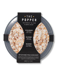 The popper, black collapsed popper viewed from top with lid on and cardboard cover with the information in white lettering.