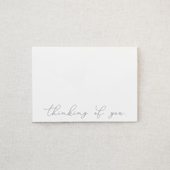 Thinking of you greeting card in grey lettering on a white background. 