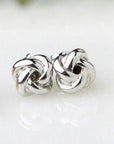 “Tie the Knot” white gold-plated earrings, featured on a marble-like background.
