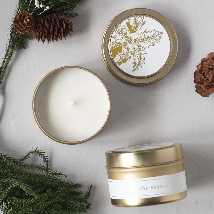 'Tis the season natural hand-poured soy candle, Hand-poured in a 4 oz. brushed gold metal tin with a white label, then on top a white label with a Christmas branch in gold. The image shows three of them: the top, the side, and an open one showing the candle with Christmas branches- decor on a white background. 