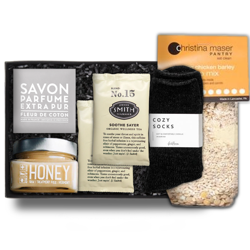 Savon Parfume Extra Pur soap in a gray wrapper. honey in a clear square jar with a silver lid, two 'No. 15' Steven Smith Teamaker packets, black 'foxblossom' cozy socks, and a Christina Maser Pantry chicken soup mixture, in a black 'foxblossom' box with black paper shread