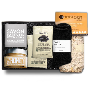 Savon Parfume Extra Pur soap in a gray wrapper. honey in a clear square jar with a silver lid, two 'No. 15' Steven Smith Teamaker packets, black 'foxblossom' cozy socks, and a Christina Maser Pantry chicken soup mixture, in a black 'foxblossom' box with black paper shread