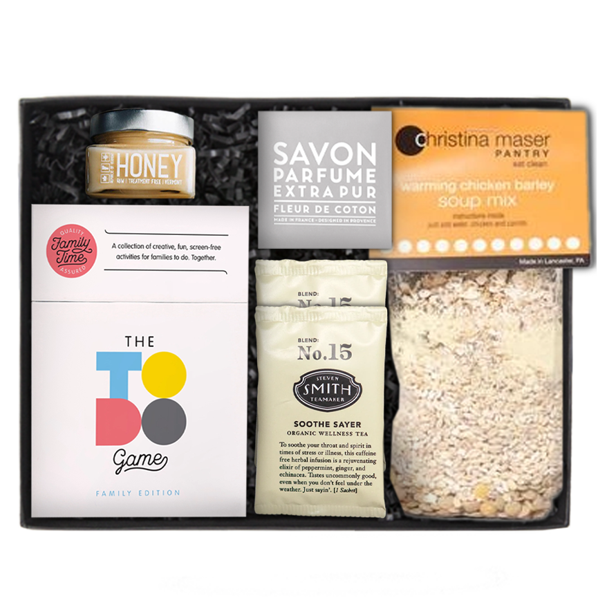 Savon Parfume Extra Pur soap in a gray wrapper. honey in a clear square jar with a silver lid, two &#39;No. 15&#39; Steven Smith Teamaker packets, The to-do game white box set, and a Christina Maser Pantry chicken soup mixture, in a black &#39;foxblossom&#39; box with black paper shread