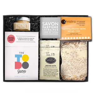 Savon Parfume Extra Pur soap in a gray wrapper. honey in a clear square jar with a silver lid, two 'No. 15' Steven Smith Teamaker packets, The to-do game white box set, and a Christina Maser Pantry chicken soup mixture, in a black 'foxblossom' box with black paper shread