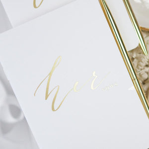 White vow book that reads "Her vows" in gold foil.