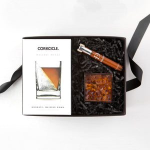 Corkcicle whiskey wedge box, clear plastic cube of bourbon bears and brown glass vial of Daneson  scotch infused toothpicks arranged in a black box with black paper shred.